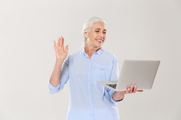 Mujer madura divertida que usa la computadora portátil aislada sobre blanco