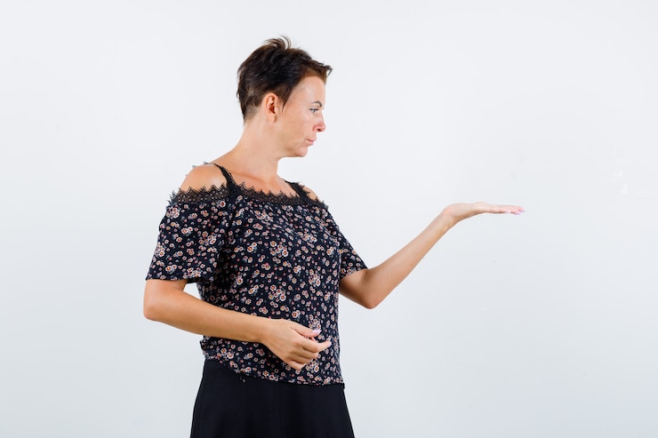 Foto gratuito mujer madura estirando la mano como sosteniendo algo y mirándolo con blusa floral y falda negra y mirando enfocado. vista frontal.