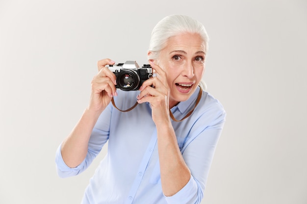 Mujer madura feliz que sostiene la cámara retra aislada