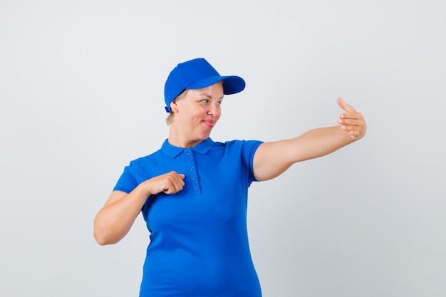 Mujer madura fingiendo tomar selfie en camiseta azul y mirando alegre