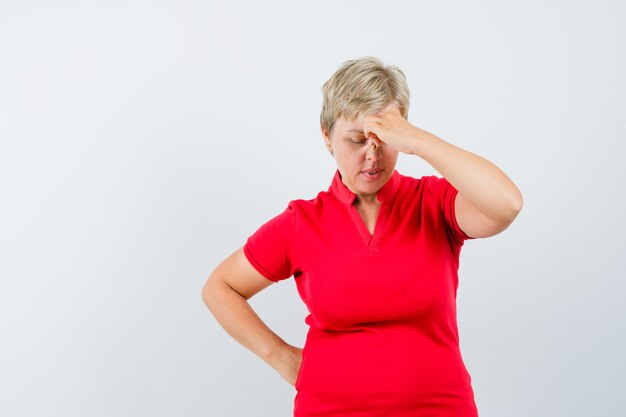 Mujer madura frotándose los ojos y la nariz en camiseta roja y mirando pensativo.