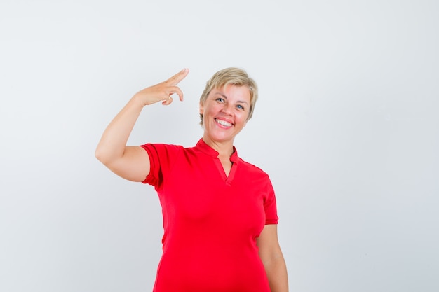 Mujer madura gesticulando con la mano y los dedos en camiseta roja y mirando confiado.