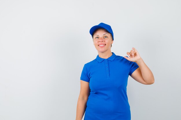 Mujer madura levantando la mano en camiseta azul y mirando contenta.