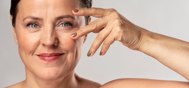 Mujer madura con maquillaje posando con las manos en la cara y mostrando las uñas