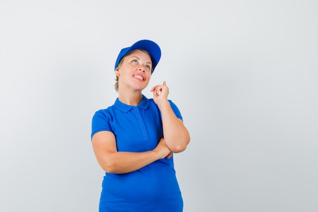 Mujer madura mirando hacia arriba con el dedo hacia arriba en camiseta azul y mirando esperanzado