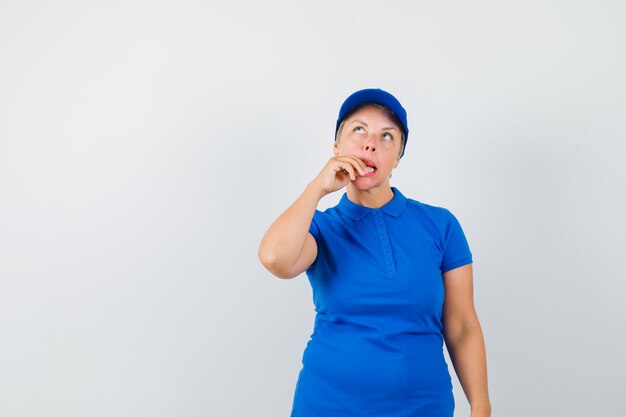 Mujer madura mordiendo los dedos en camiseta y mirando confundido