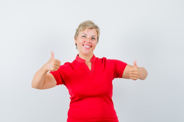 Mujer madura mostrando doble pulgar hacia arriba en camiseta roja y mirando confiado.