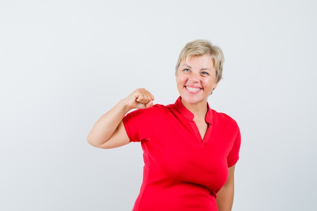 Mujer madura mostrando gesto de éxito en camiseta roja y mirando alegre