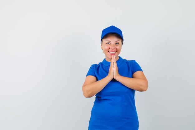 Mujer madura mostrando gesto namaste en camiseta azul y mirando feliz.