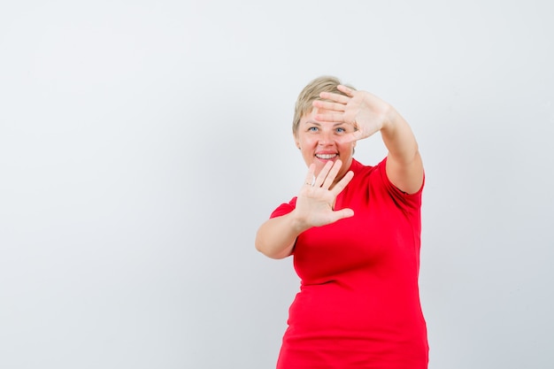 Mujer madura mostrando gesto de parada en camiseta roja y mirando avergonzado.