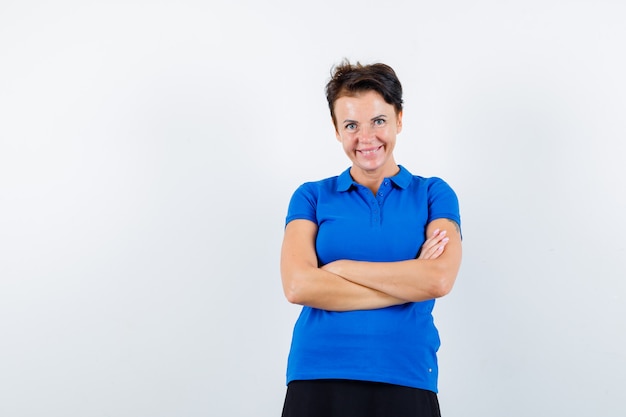 Mujer madura de pie con los brazos cruzados en camiseta azul y mirando feliz. vista frontal.