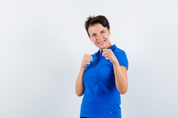 Mujer madura de pie en pose de lucha en camiseta azul y mirando confiado. vista frontal.