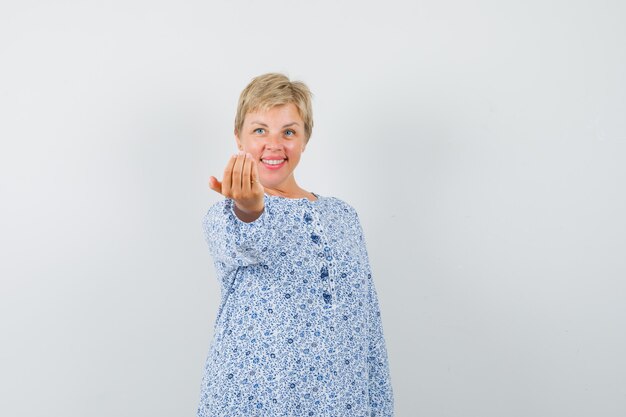 Mujer madura que invita a entrar en camisa y luce alegre.