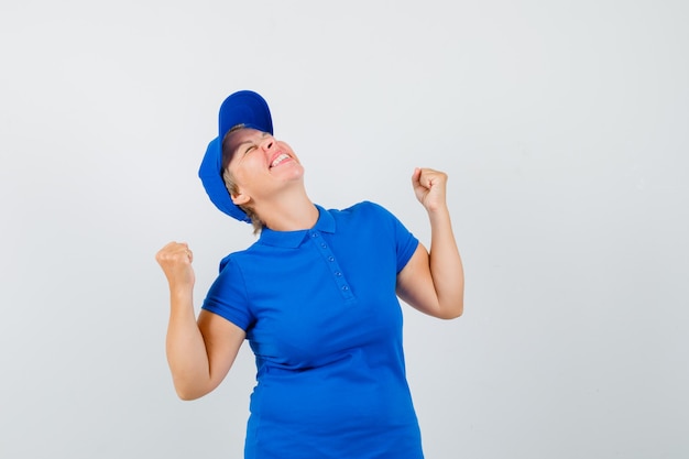 Mujer madura que muestra el gesto del ganador en camiseta azul y parece feliz.