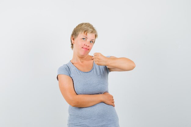 Mujer madura que muestra el puño cerrado en camiseta gris y parece seguro.