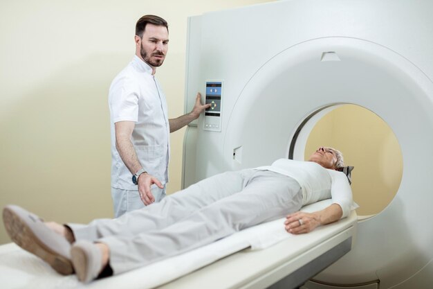 Mujer madura que se somete a una tomografía computarizada mientras un técnico médico supervisa el procedimiento en el hospital