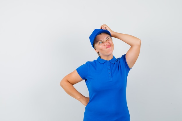 Mujer madura rascándose la cabeza con camiseta azul y mirando pensativo.