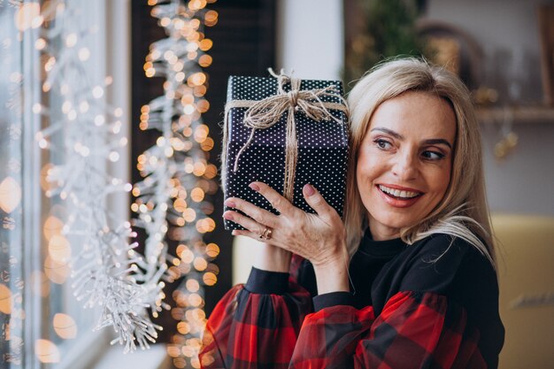 Mujer madura con regalo de navidad por bthe ventana