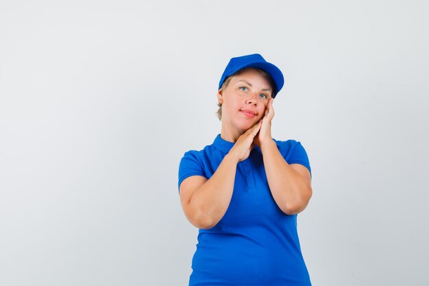 Mujer madura revisando la piel de su rostro en camiseta azul y luciendo elegante.