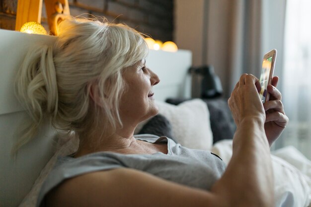 Mujer madura con smartphone en la cama