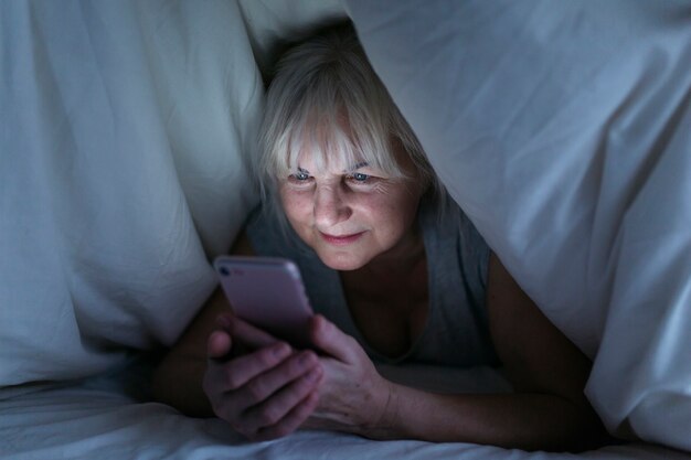Mujer madura con smartphone debajo de la manta