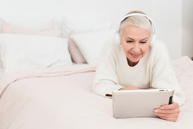 Mujer madura sonriendo y mirando la tableta en la cama con espacio de copia