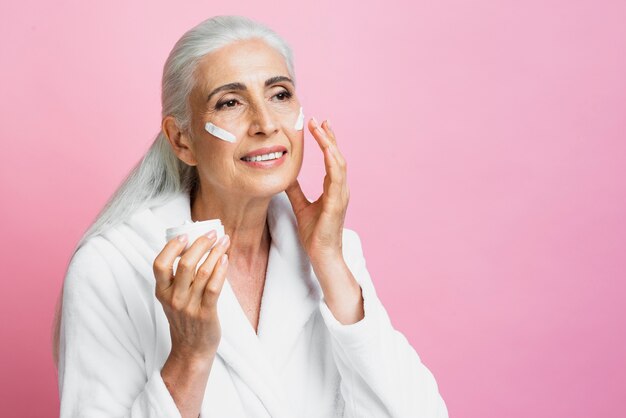 Mujer madura sonriente aplicando cuidado de la piel