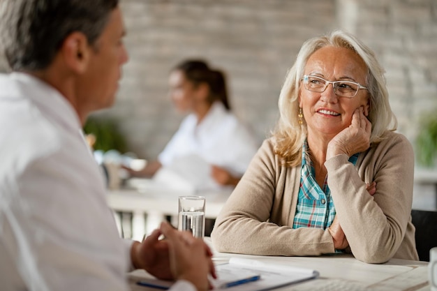 Mujer madura sonriente está hablando con un médico durante el asesoramiento en la clínica médica