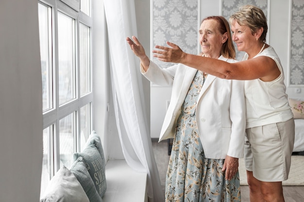 Mujer madura sonriente mostrando algo desde la ventana