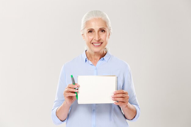 Mujer madura sonriente que muestra el cuaderno con espacio de copia para texto aislado