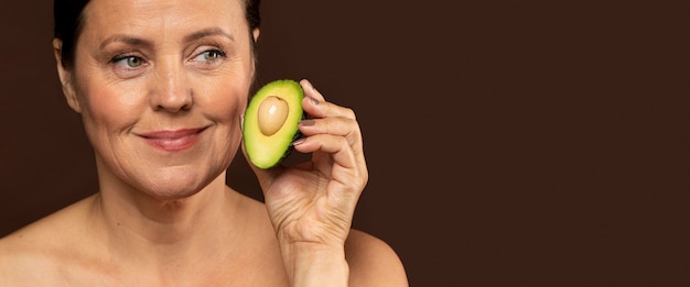 Mujer madura sonriente sosteniendo la mitad de un aguacate con espacio de copia