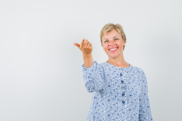 Mujer madura en vestido invitando a venir y mirando alegre