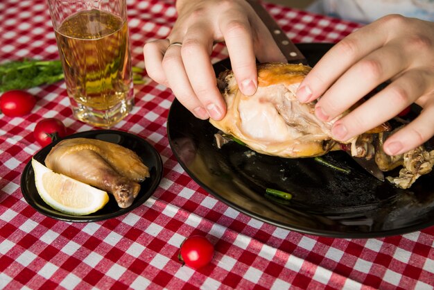 Mujer mano comiendo pollo asado con un vaso de cerveza mientras cenando