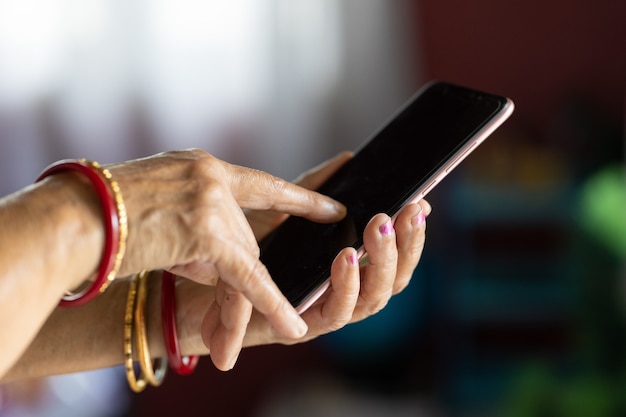 Mujer con manos arrugadas usando un teléfono inteligente con un fondo borroso