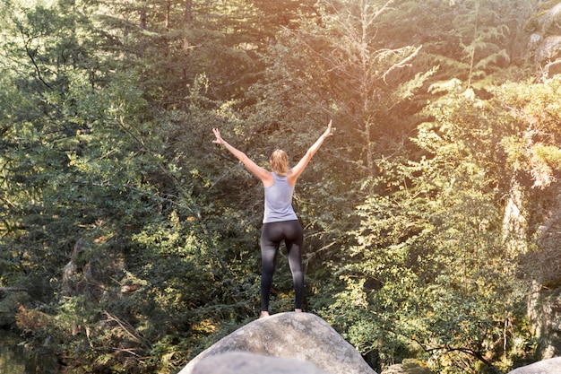 Foto gratuita mujer con las manos levantadas en piedra cerca del bosque