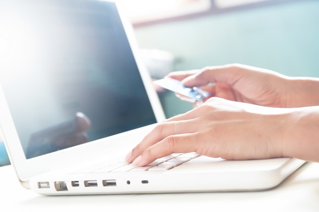 Mujer manos en el teclado de la computadora portátil y la celebración de la tarjeta de crédito, concepto de compras en línea con copia espacio