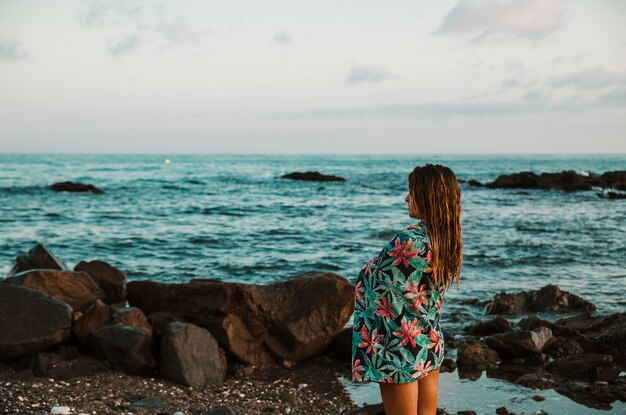 Mujer en manta de pie en la orilla del mar