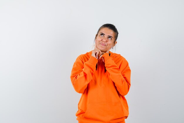 Mujer manteniendo los dedos en las mejillas en sudadera con capucha naranja y luciendo esperanzada