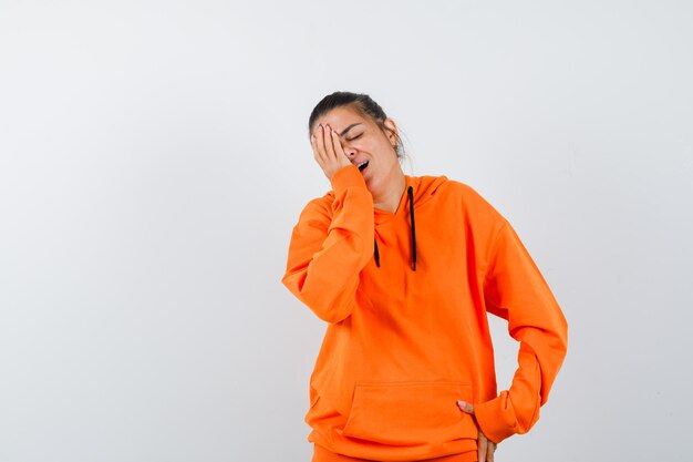 Mujer manteniendo la mano en la cara con sudadera con capucha naranja y mirando feliz