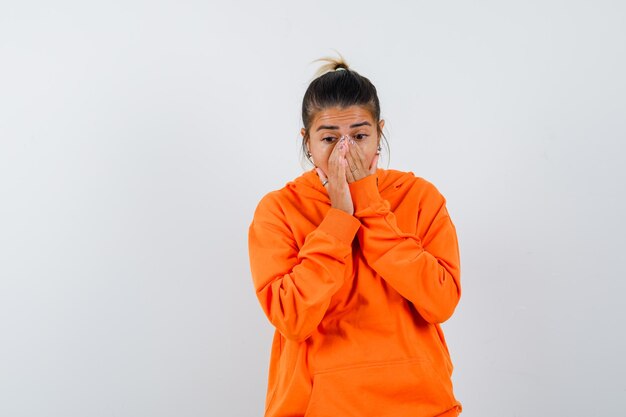 Mujer manteniendo las manos en la boca en sudadera con capucha naranja y mirando ansiosa