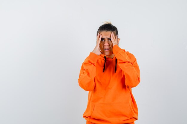 Mujer manteniendo las manos en la cabeza con una sudadera con capucha naranja y mirando triste