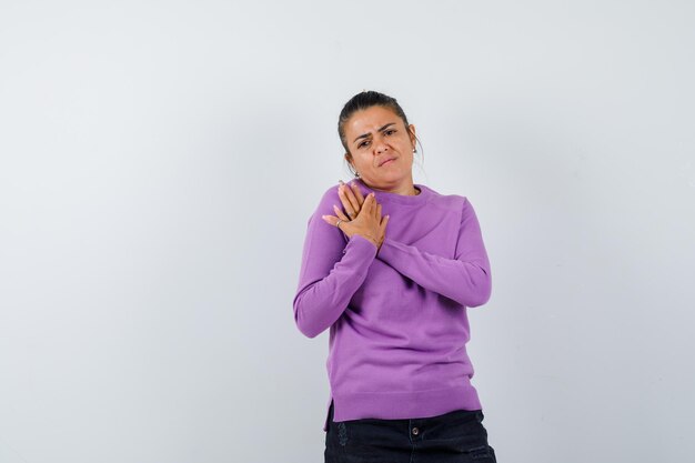 Mujer manteniendo las manos sobre el pecho en una blusa de lana y luciendo triste