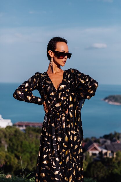 Mujer con maquillaje de bronce en vestido negro dorado posando en seascape