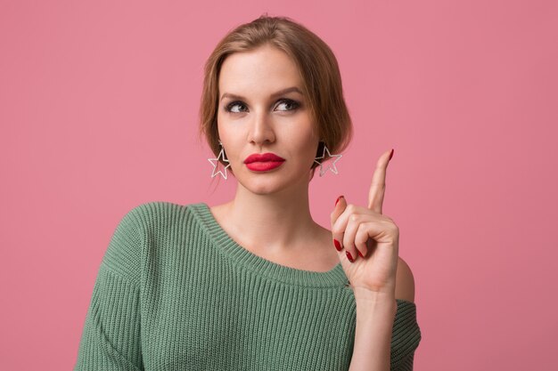 mujer con maquillaje elegante, labios rojos, suéter verde posando en rosa