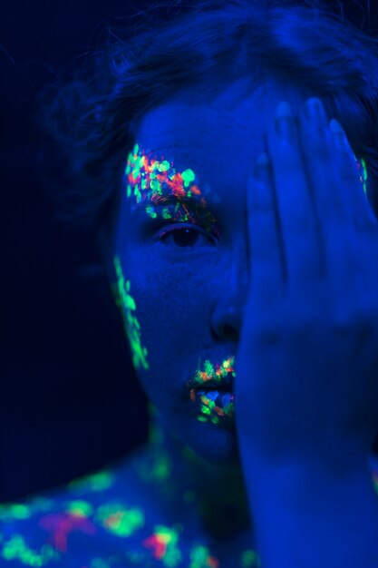 Mujer con maquillaje fluorescente y mano en la cara