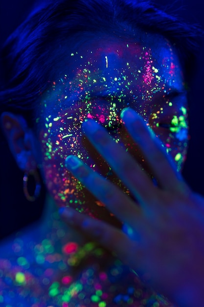 Foto gratuita mujer con maquillaje fluorescente y mano en la cara