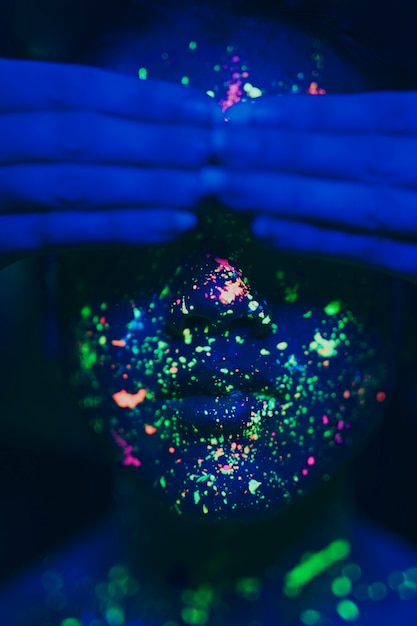 Mujer con maquillaje fluorescente y manos en los ojos