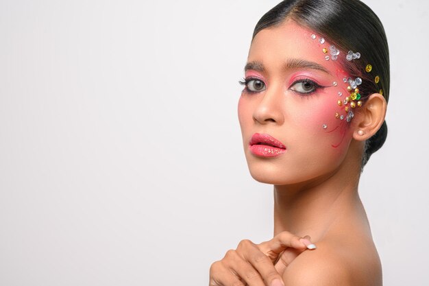 Mujer con maquillaje rosa y adornos en su rostro aislado en blanco