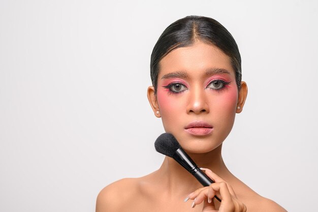 Mujer con maquillaje rosa y sosteniendo un pincel de rubor aislado en blanco