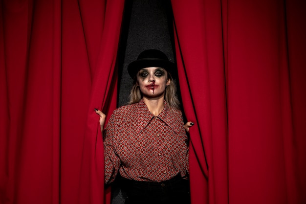 Mujer de maquillaje sosteniendo una cortina roja de teatro